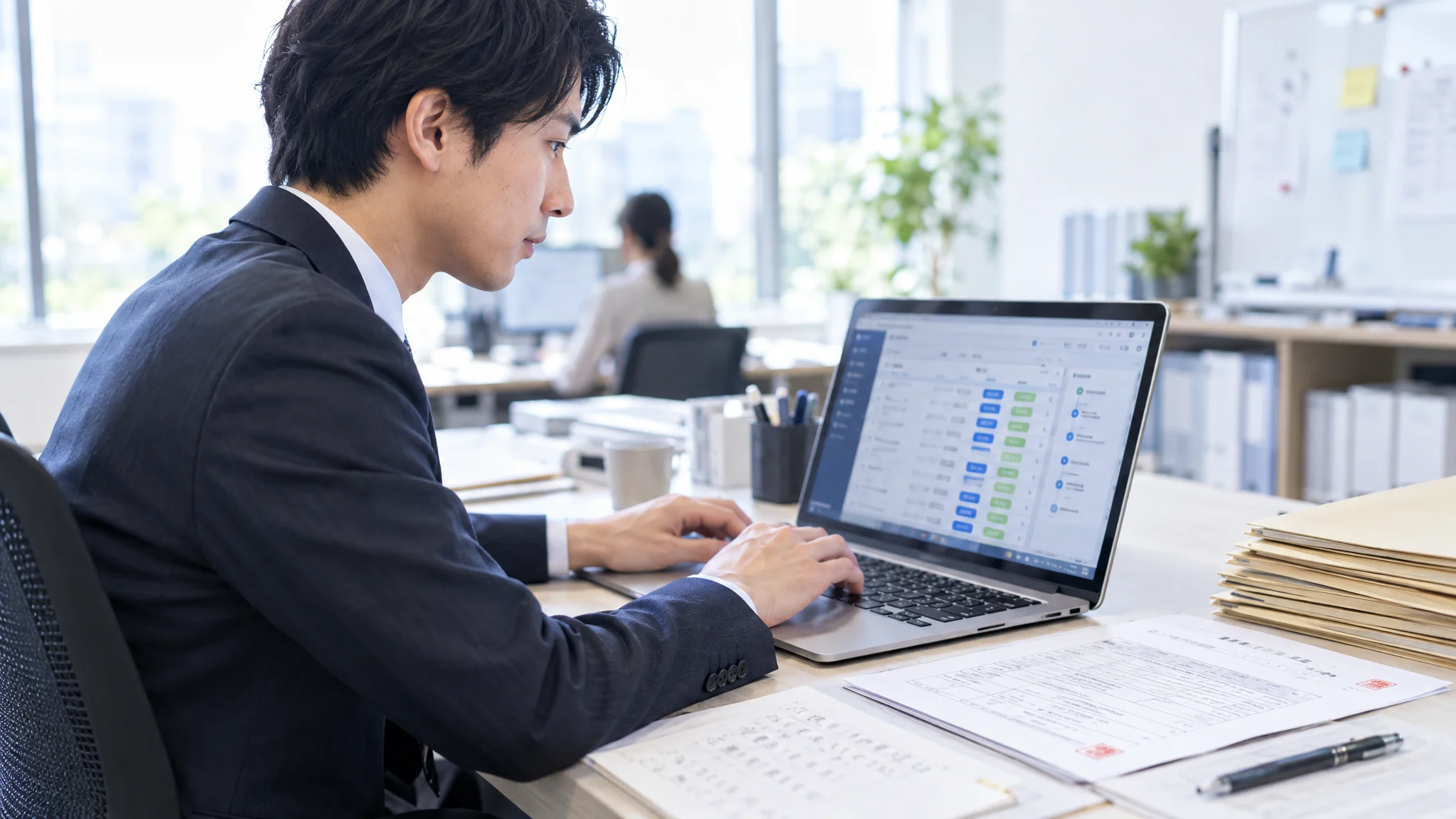 日本語のビジネス文書が並ぶデスクの上で、日本人の職員がノートパソコンを操作している。視線は画面に向けられており、キーボードを打つ手元が写っている。画面には自治体向けのワークフロー管理システムが表示されており、未処理・処理済みのステータスが並んでいる。周囲には特定の名称が入っていない無地のファイルや帳票が整然と置かれている。